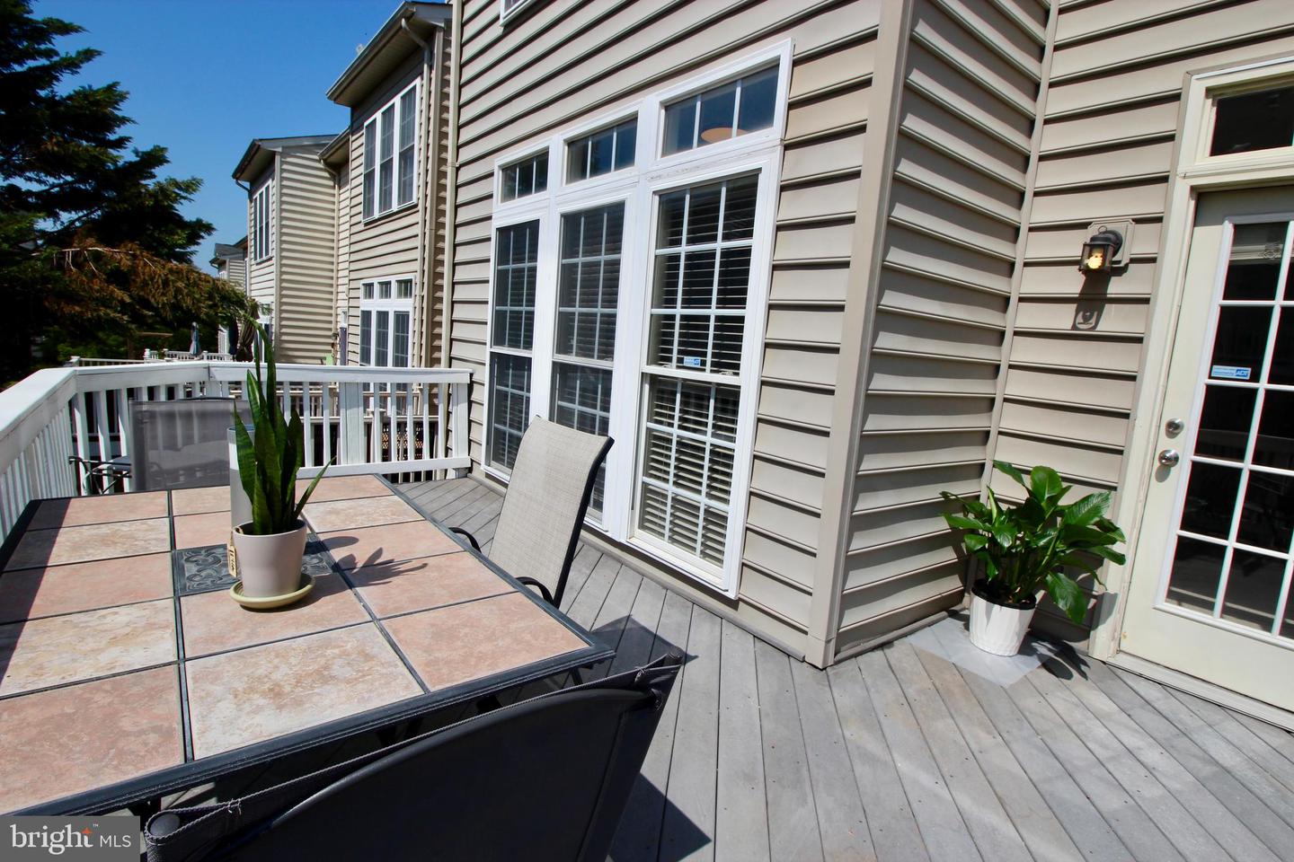 Outdoor deck with a tiled table, chairs, and potted plants beside the house.
