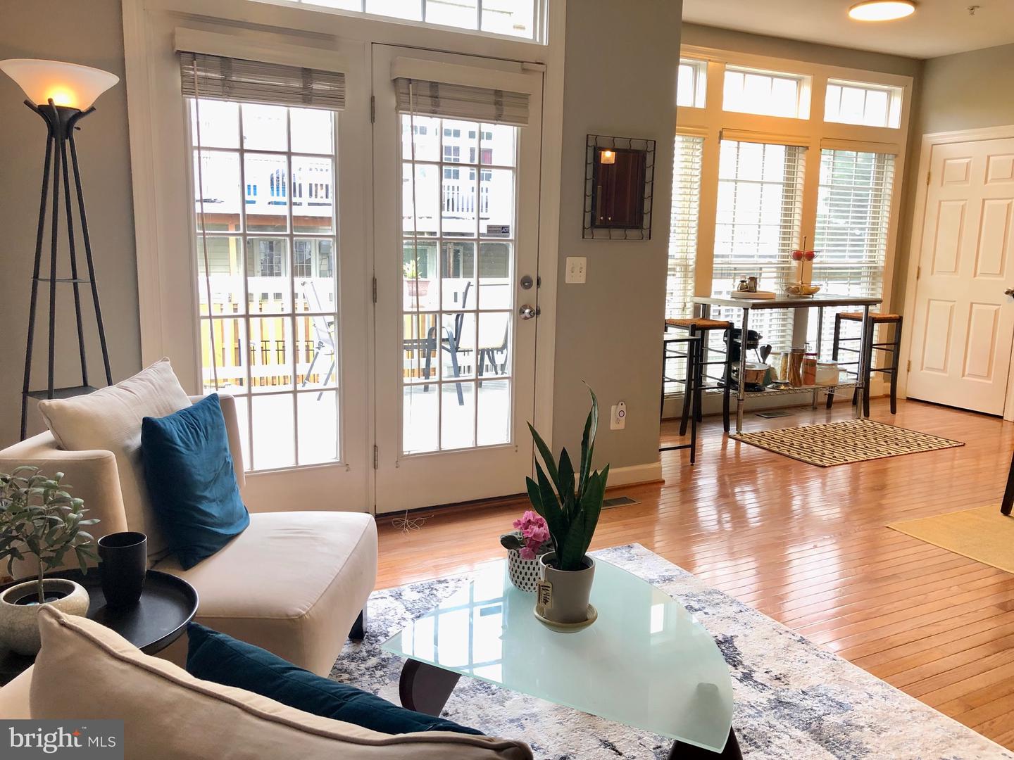 Living and dining area with hardwood floors, white seating, and French doors opening to a balcony.