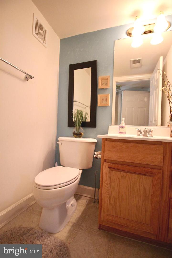Bathroom with an oak vanity, large mirror, and blue accent wall beside a white toilet.