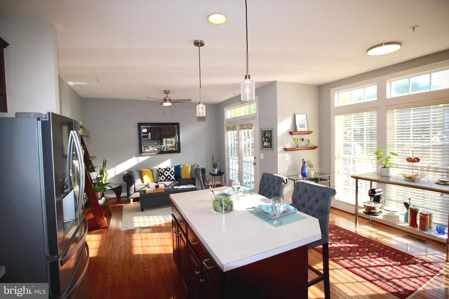 Open-plan kitchen and living room with a large island, hardwood floors, and sunny windows.