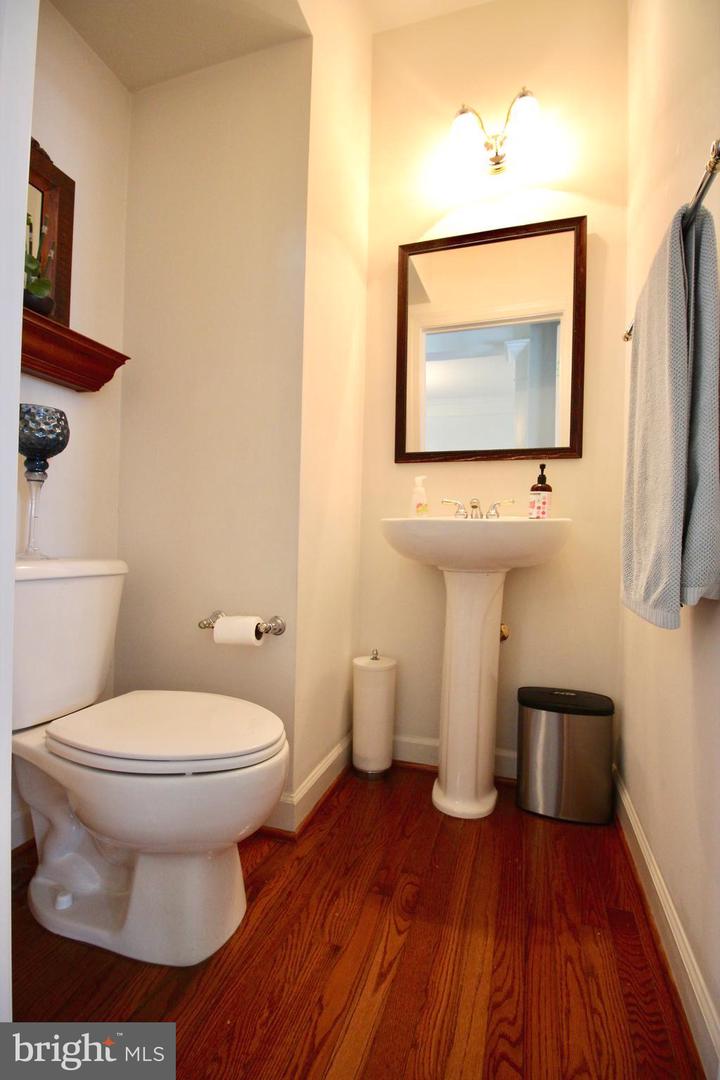 Powder room with a pedestal sink, framed mirror, white toilet, and dark wood flooring.