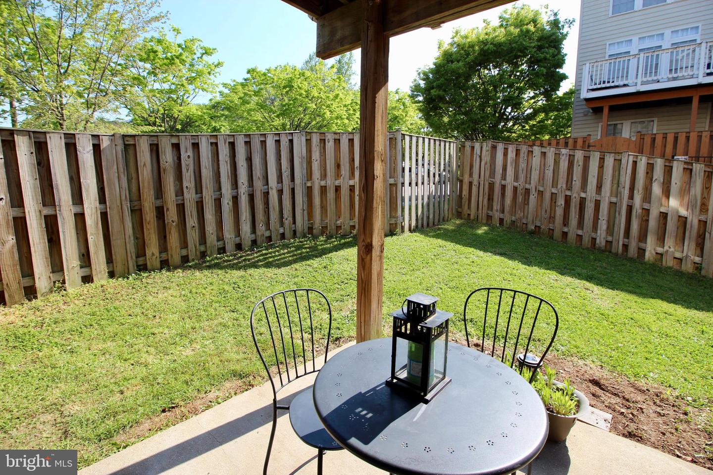 Backyard patio with a round table beneath a wooden pergola, opening onto a fenced lawn.