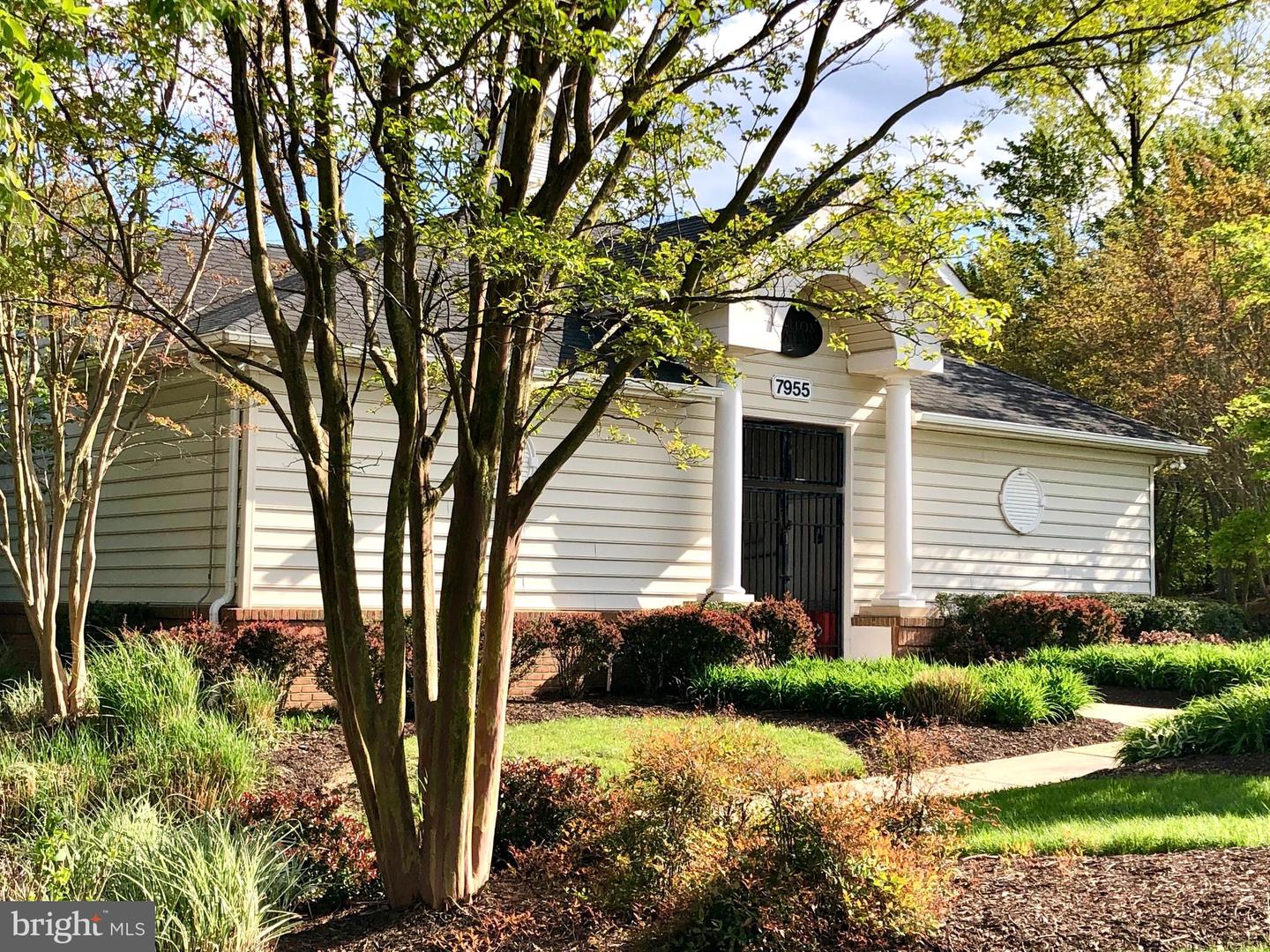 White-sided building with a columned entrance, partly screened by mature trees and landscaped grounds.