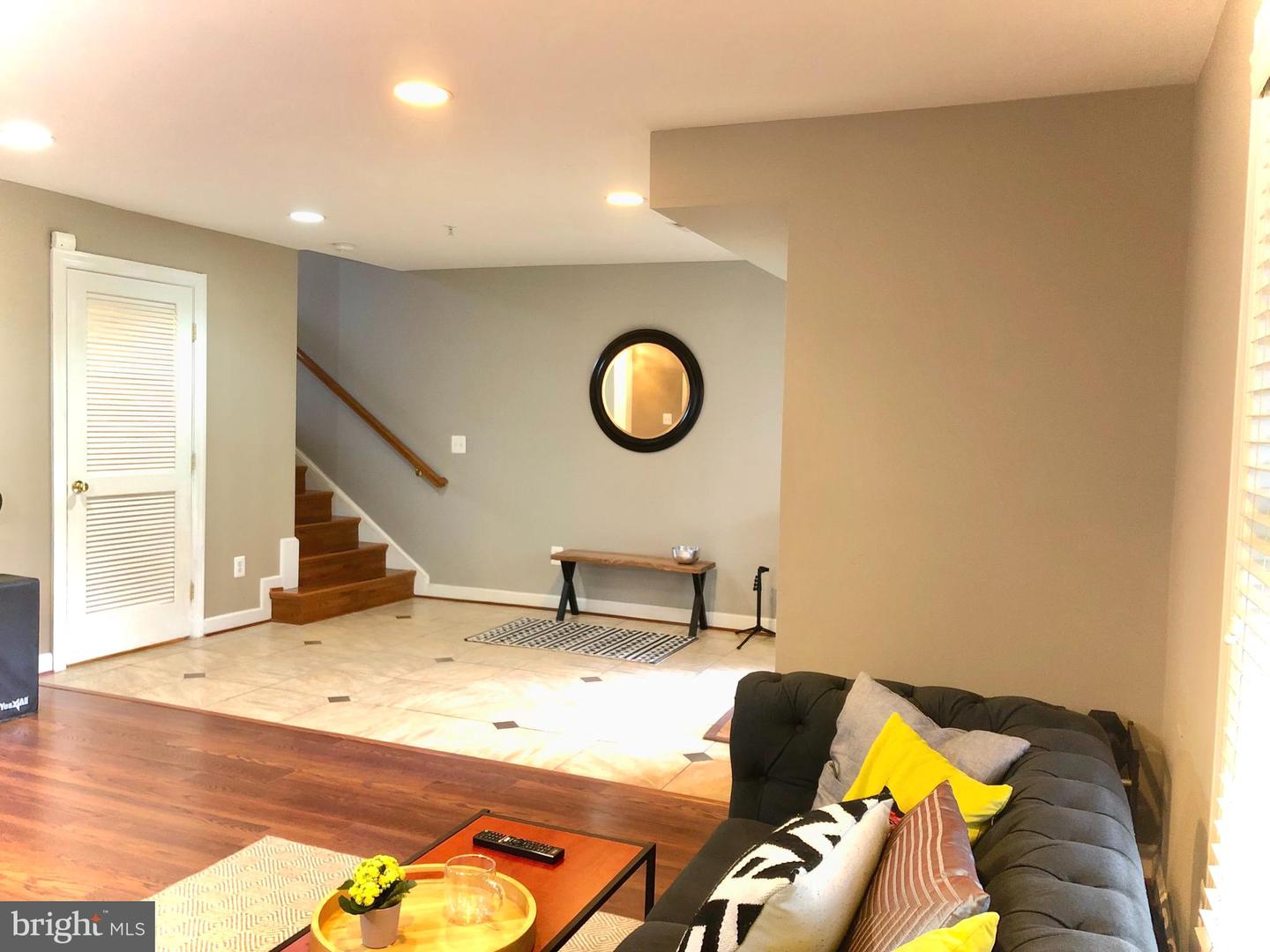 Furnished living room with a dark sofa, tiled entry, and staircase with a wooden handrail.