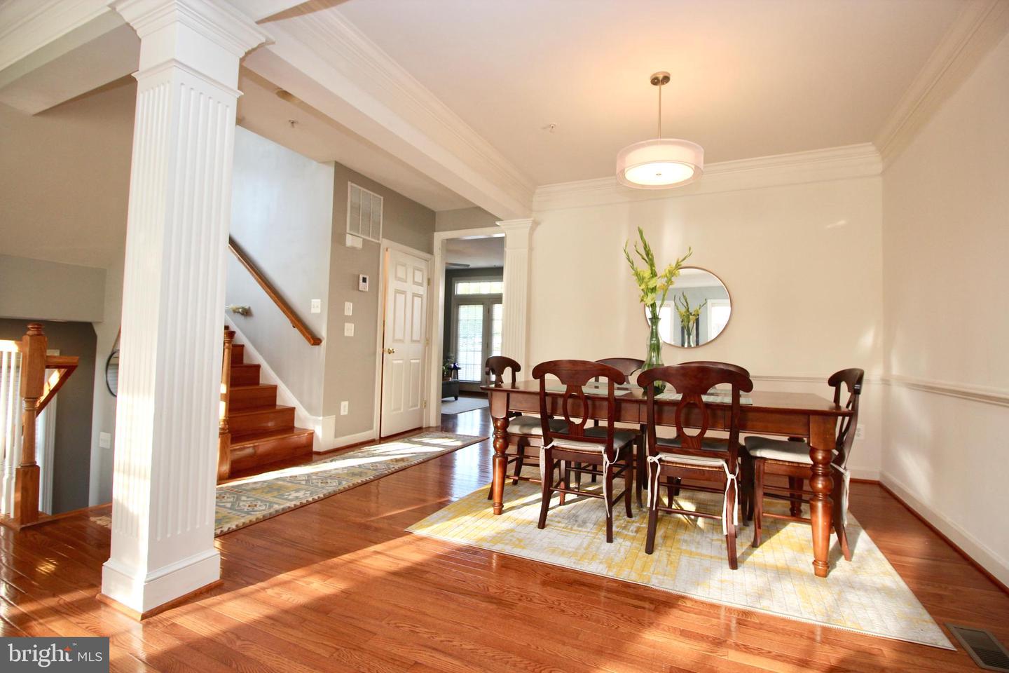 Dining room with a dark wood table, hardwood floors, and a staircase framed by white columns.