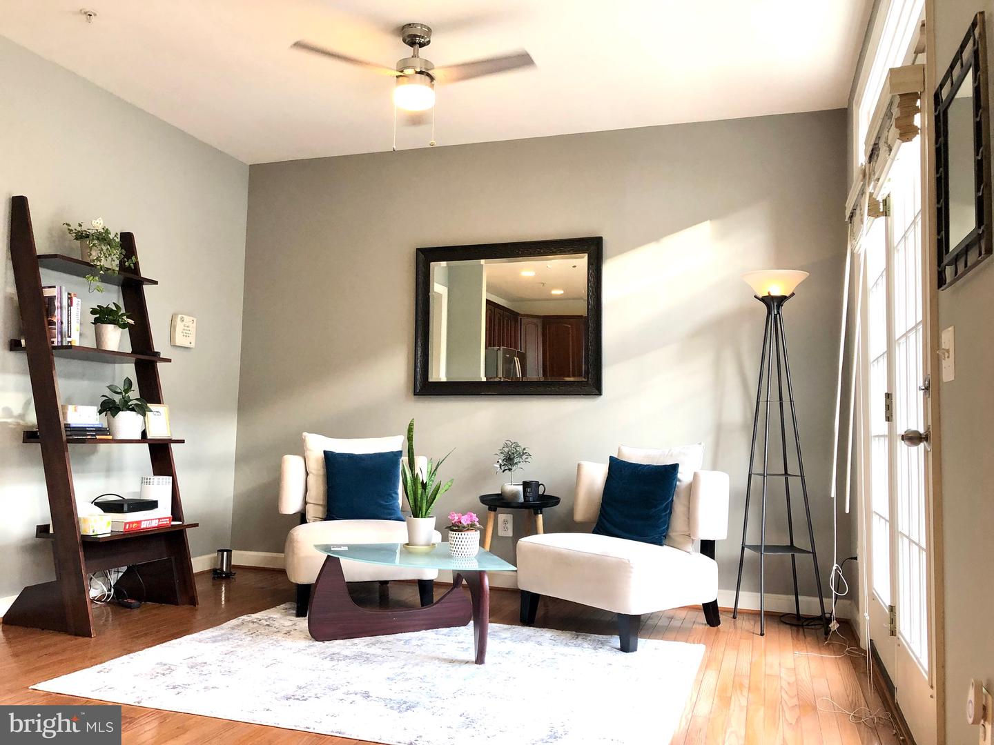 Staged living room with white armchairs, navy cushions, hardwood floors, and tall glass doors.