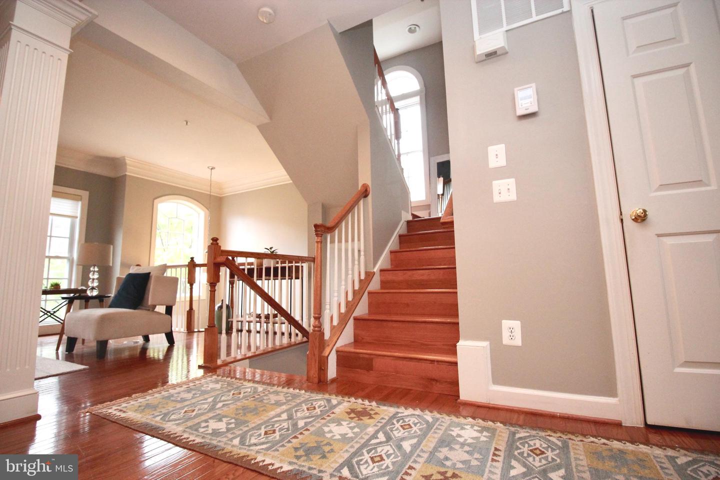 Foyer with a hardwood staircase, patterned rug, and sitting area by arched windows.