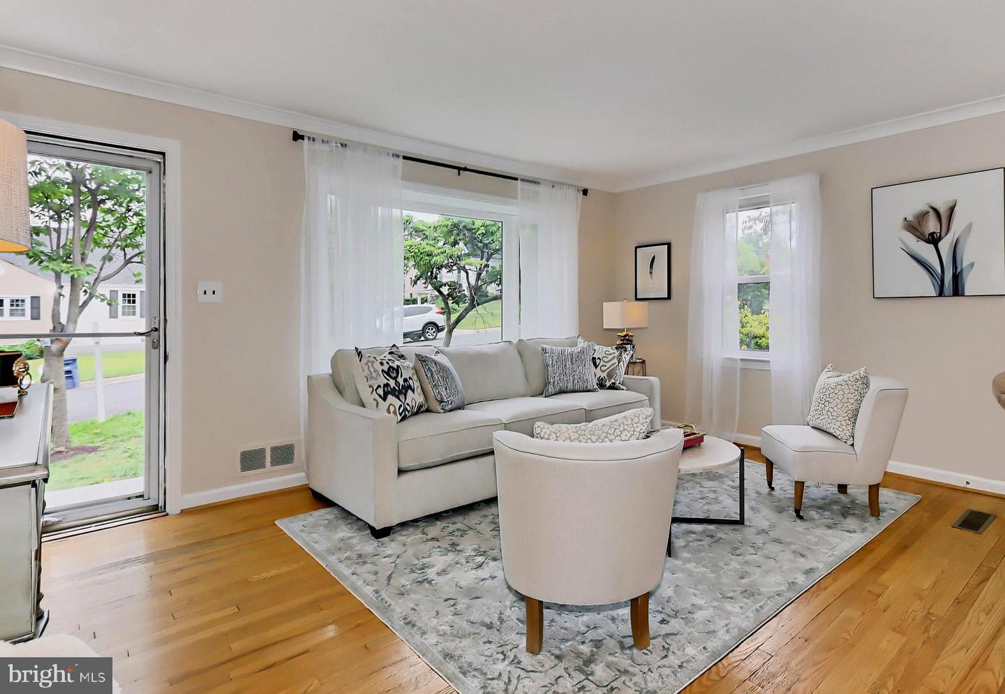 Staged living room with a light sofa, patterned rug, hardwood floors, and large windows.