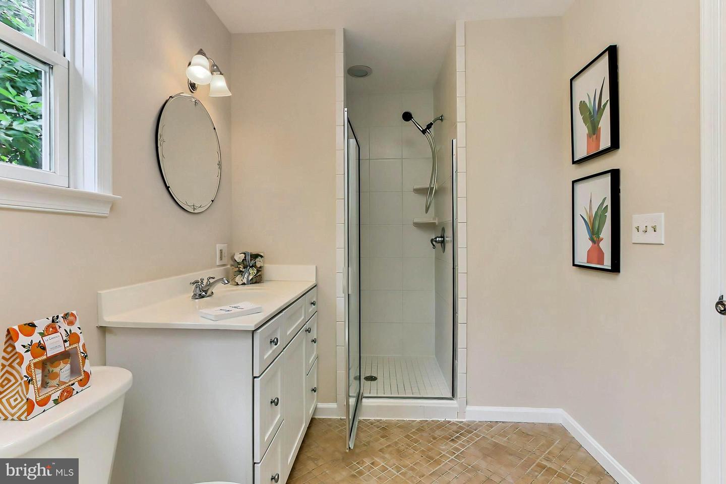 Bathroom with a white vanity and glass-enclosed shower, featuring tan patterned floor tile.