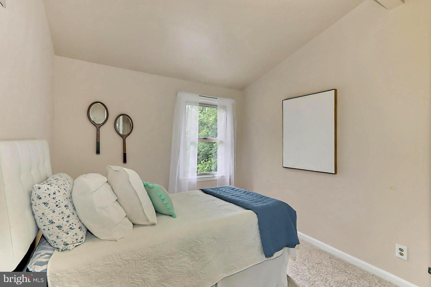 Furnished bedroom with a white bed, blue throw, and tennis-racket-shaped mirrors on the wall.