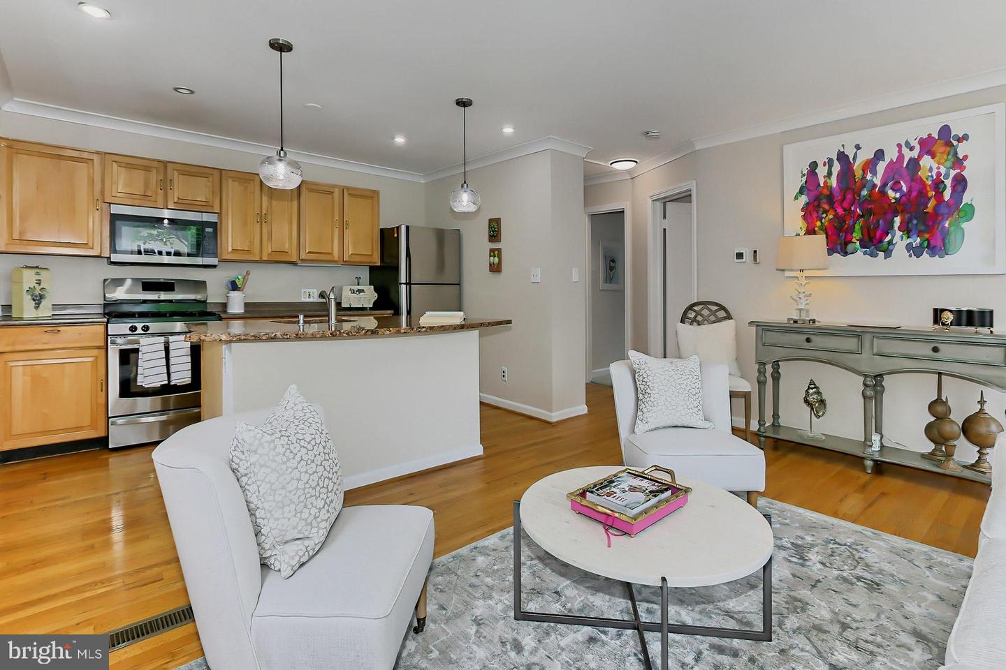 Open-plan kitchen and living area with wood cabinets, stainless appliances, and white seating.