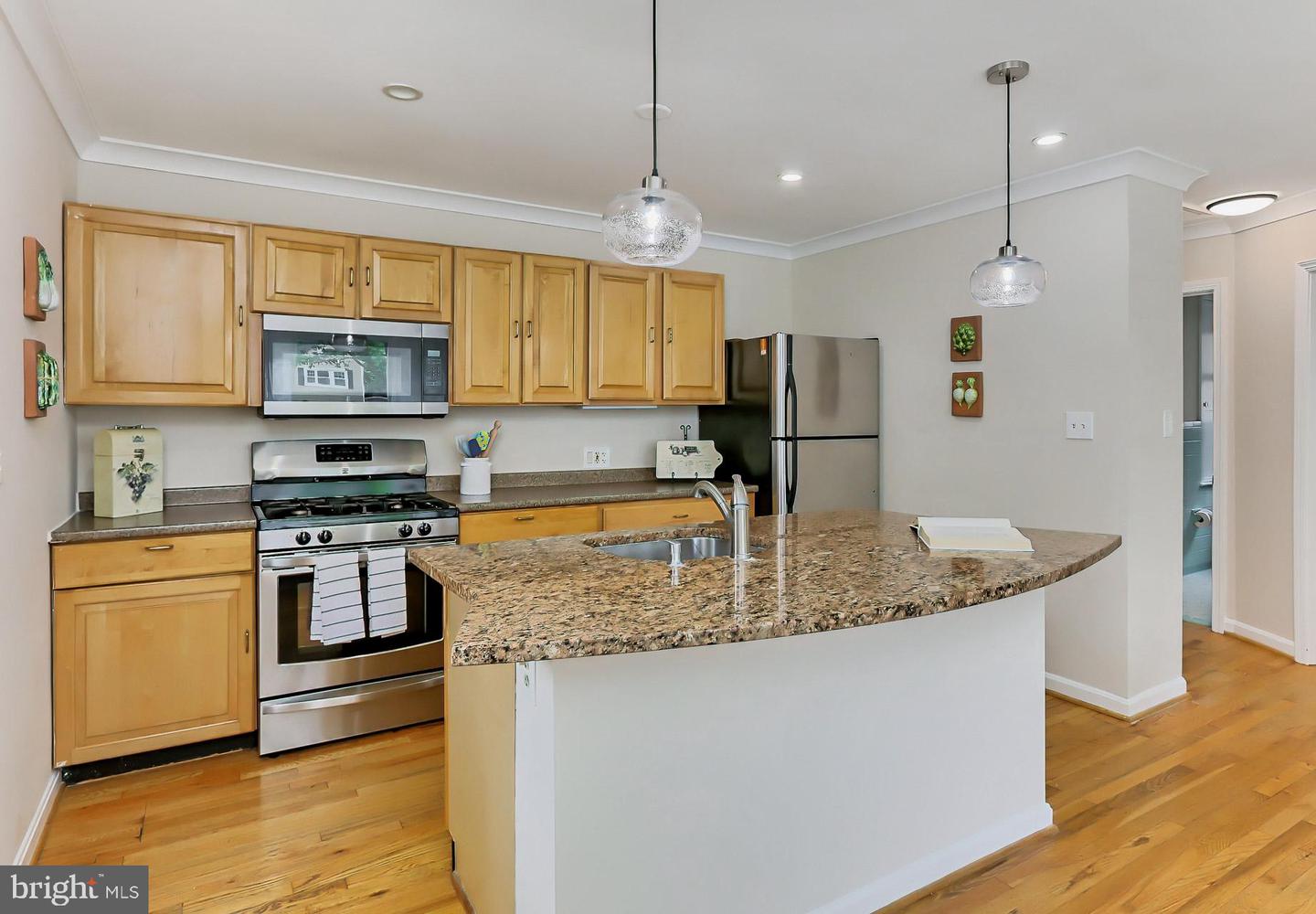 Kitchen with honey-colored cabinets, stainless steel appliances, and a large granite island with a sink.
