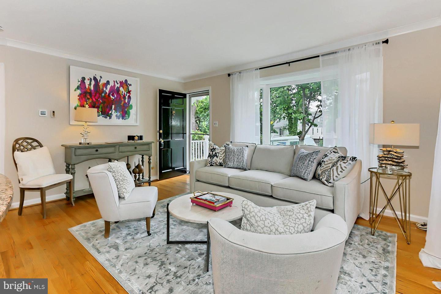 Staged living room with a light sofa, colorful wall art, hardwood floors, and large windows.