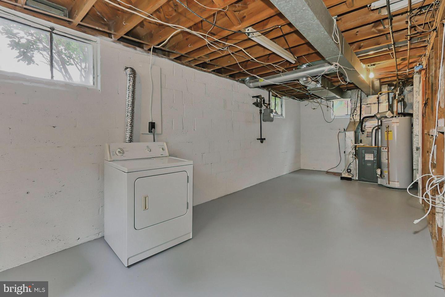 Unfinished basement laundry area with a dryer, exposed ceiling joists, and utility equipment.