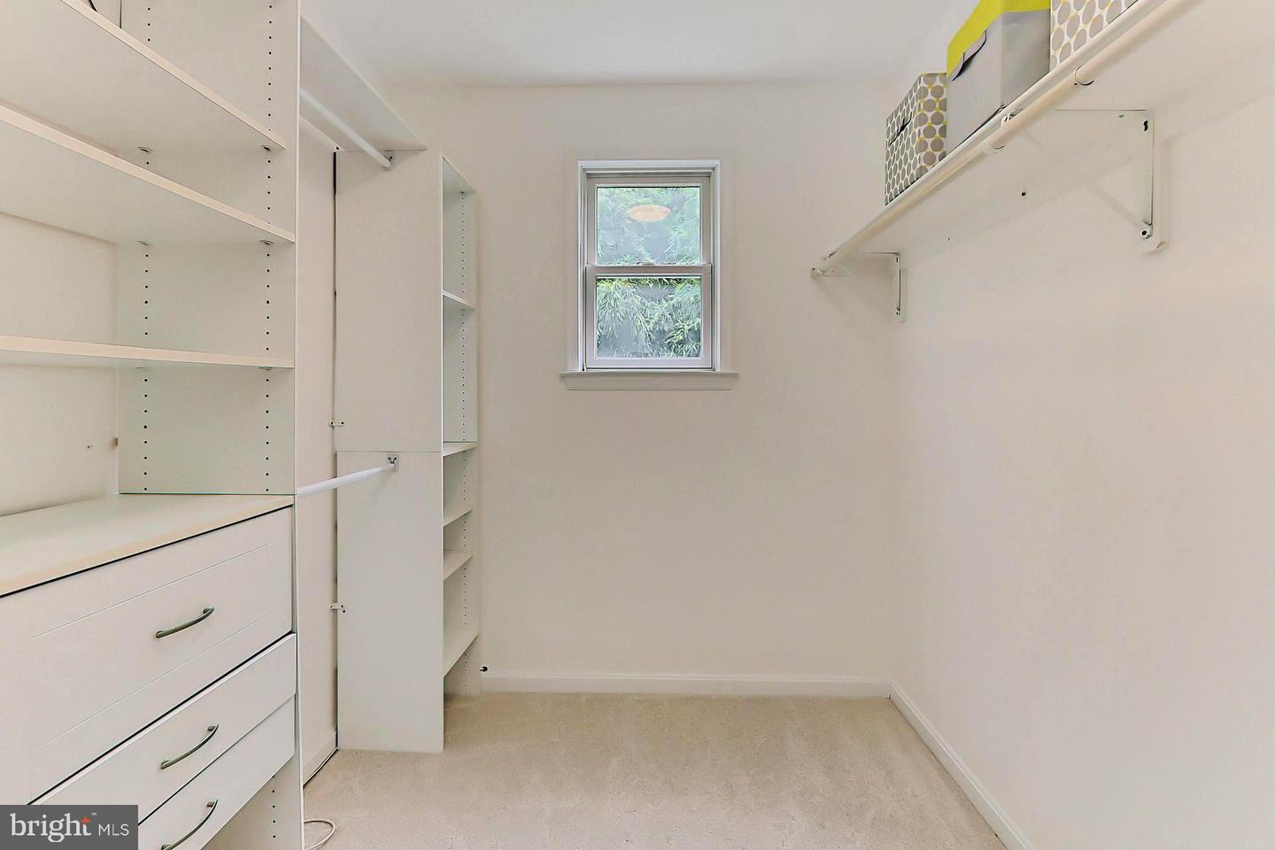 Walk-in closet with white built-in shelving and drawers, hanging rods, and a window.