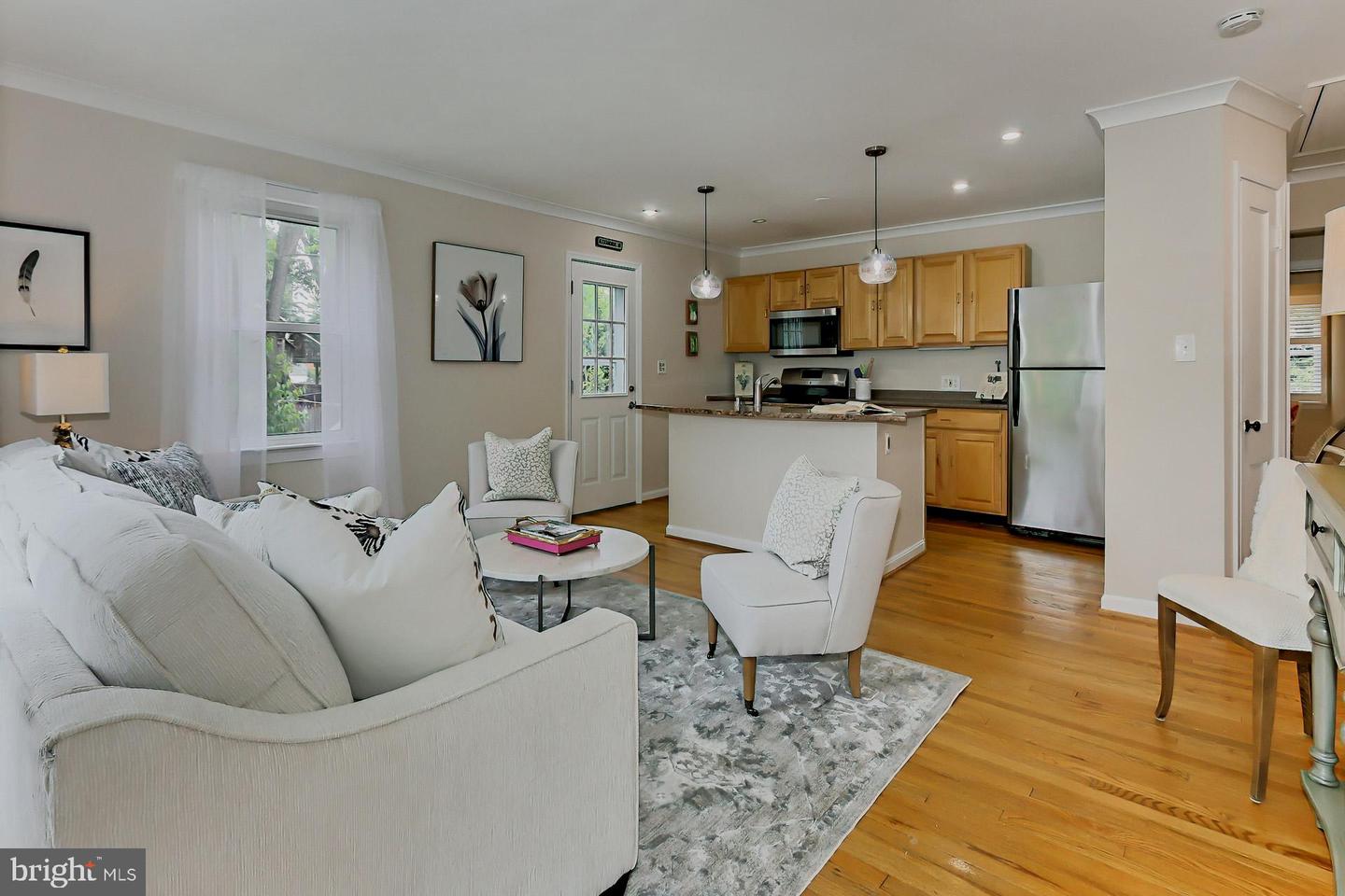 Open living room and kitchen with white seating, hardwood floors, and honey-colored cabinets.
