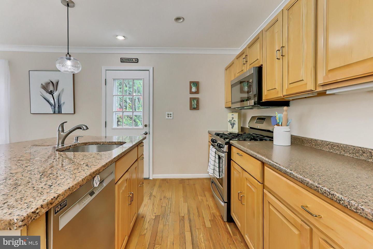 Kitchen with honey-colored cabinets, granite counters, stainless steel appliances, and hardwood floors.