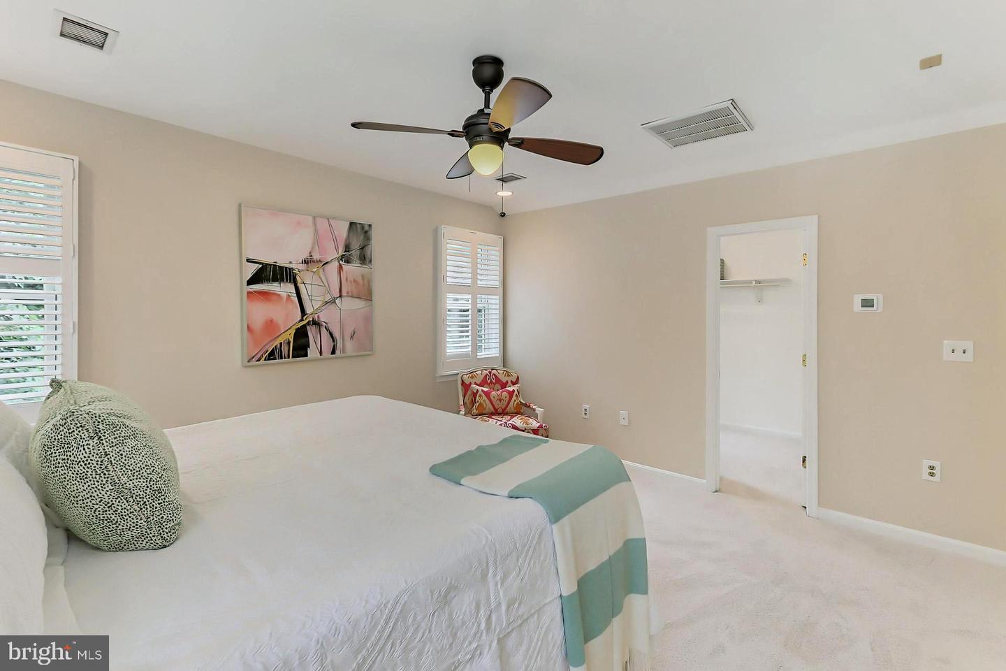 Furnished bedroom with plantation shutters, a ceiling fan, and abstract wall art.