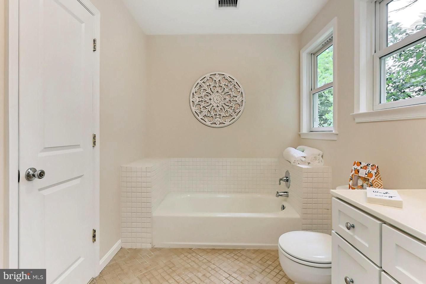 Bathroom with a tiled bathtub surround, two windows, white vanity, and round wall decoration.