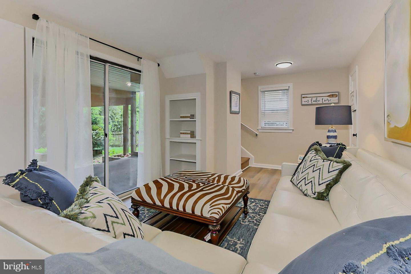 Living room with white sectional sofas, a patterned ottoman, and sliding glass doors to a covered patio.