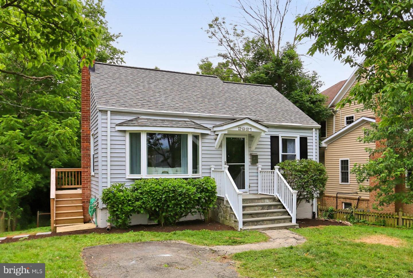 Light gray house with white front steps, a large picture window, and mature greenery.