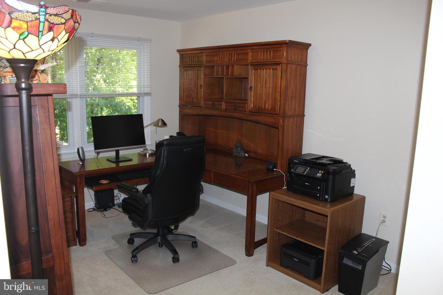 Home office with a wooden desk and hutch, black chair, and printer.