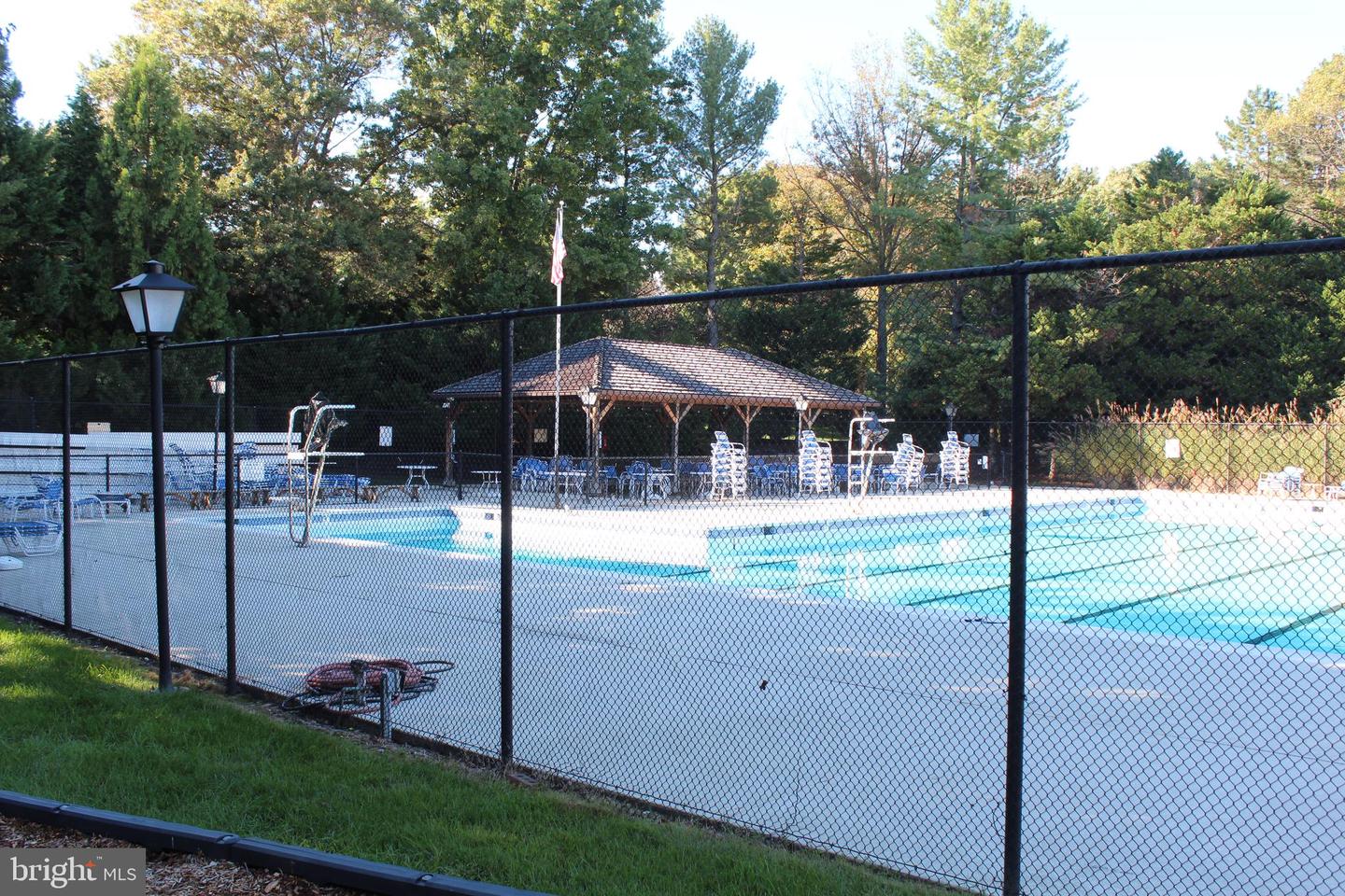 Community swimming pool behind a black fence, with a covered pavilion and lounge chairs.