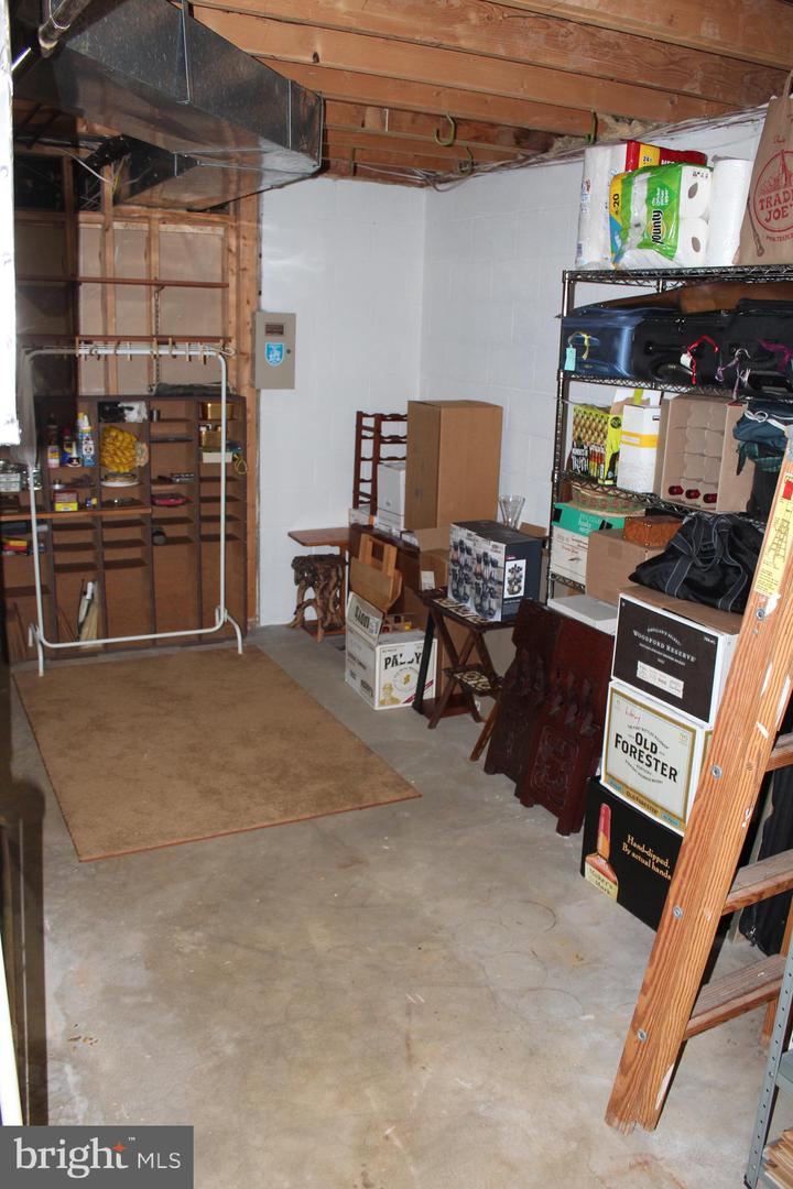 Unfinished basement storage room with exposed joists, concrete floor, and shelves filled with stored items.