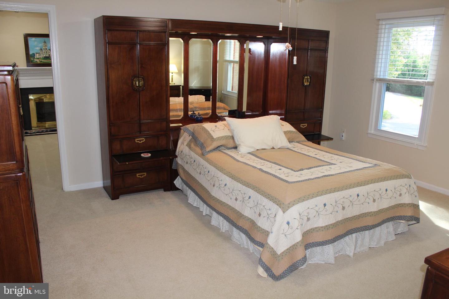 Bedroom with a patterned bedspread, dark wood mirrored cabinets, and beige carpet.
