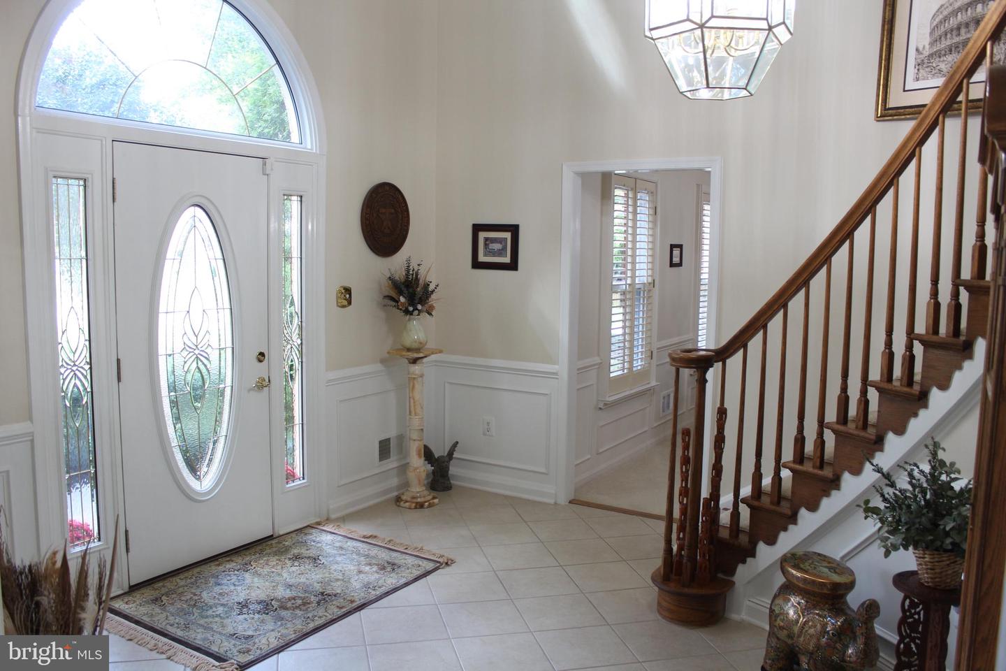 Entry foyer with an oval leaded-glass front door, arched transom, tiled floor, and wooden staircase.