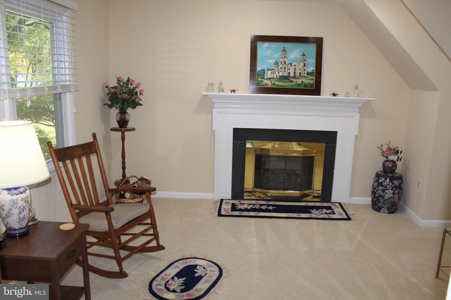 Living room with a white mantel fireplace, brass trim, and wooden rocking chair beside a large window.