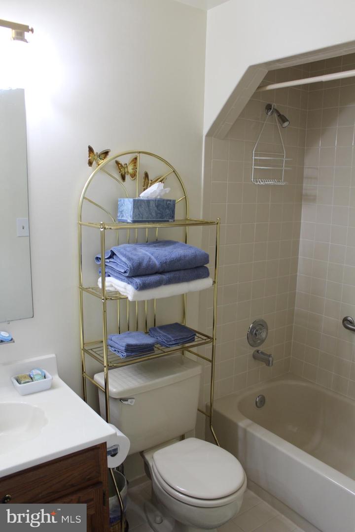 Bathroom with beige tiled tub surround and a gold towel shelf above the toilet.