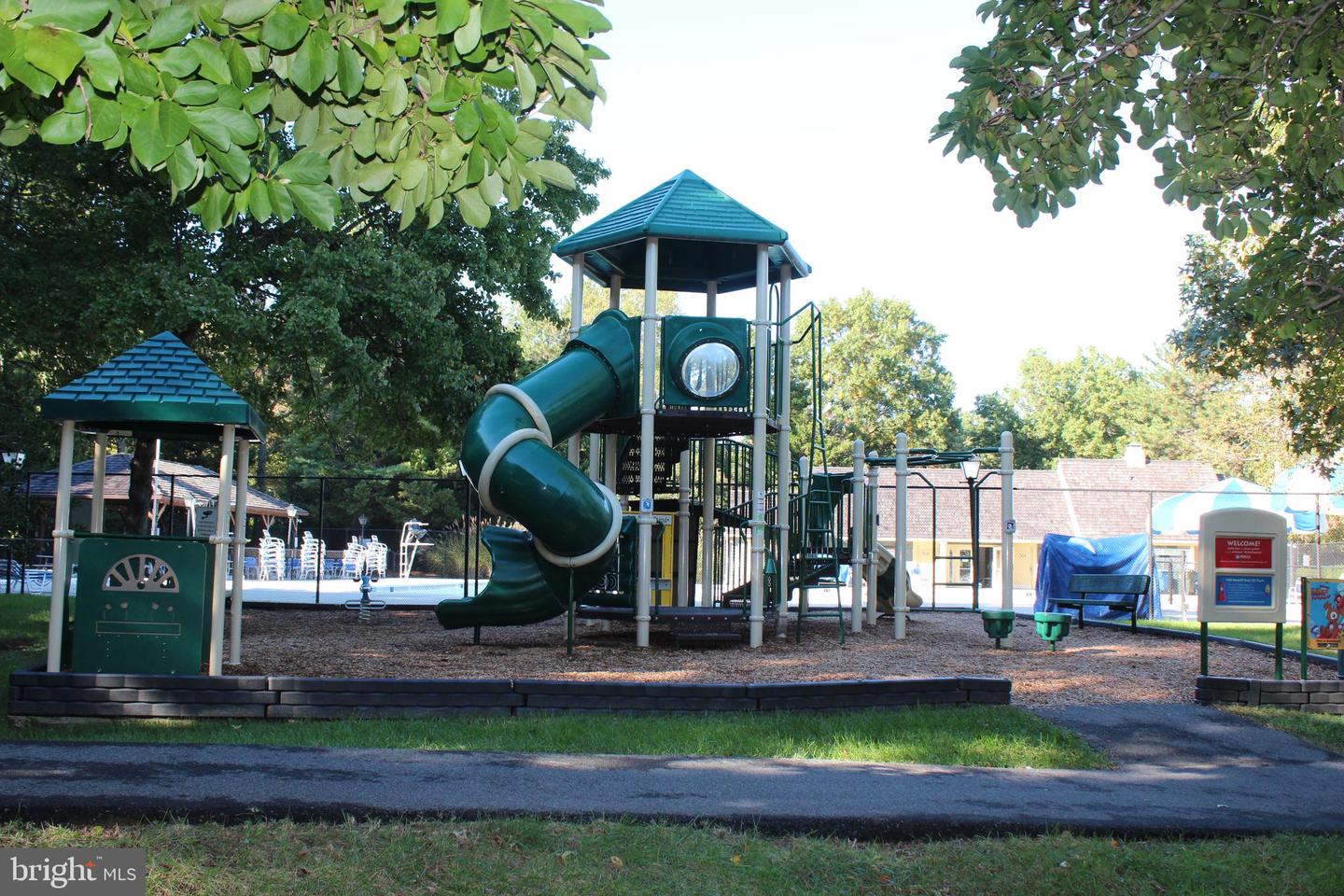 Community playground with a tall green tube slide beside a fenced pool area.