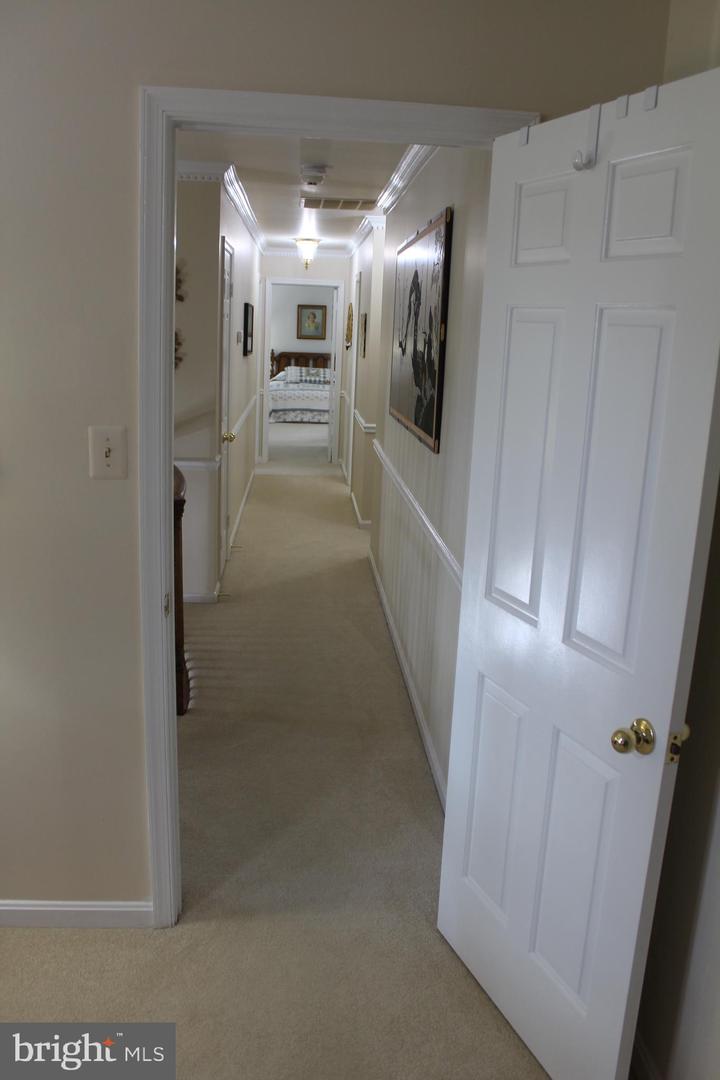 Carpeted hallway with white wainscoting, framed artwork, and an open door toward a bedroom.