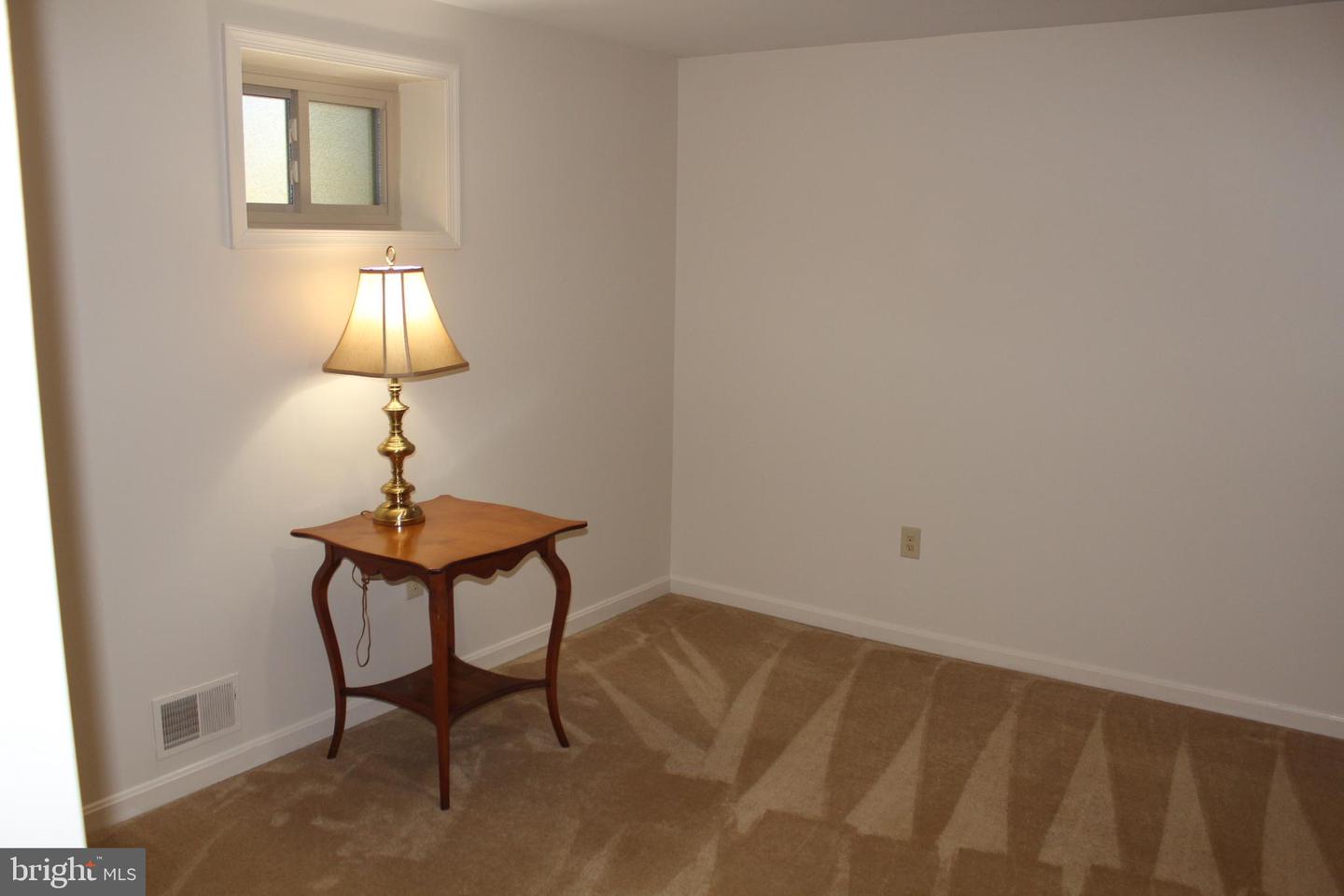 Carpeted room with a high window and a wooden table topped by a lit brass lamp.
