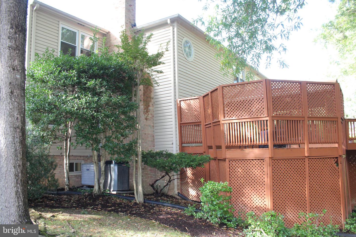 Rear of a two-story house with a large elevated lattice-sided deck and leafy landscaping.