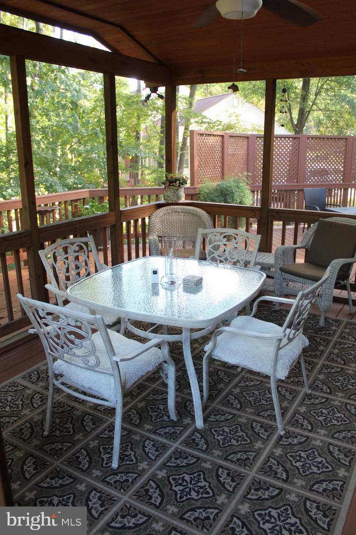 Screened porch with white patio dining set, patterned tile floor, and leafy views.