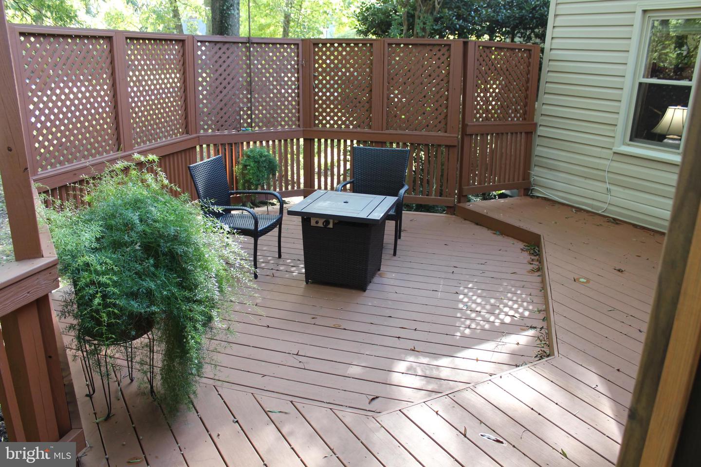Wooden deck with lattice privacy fencing, woven chairs, a table, and potted greenery.
