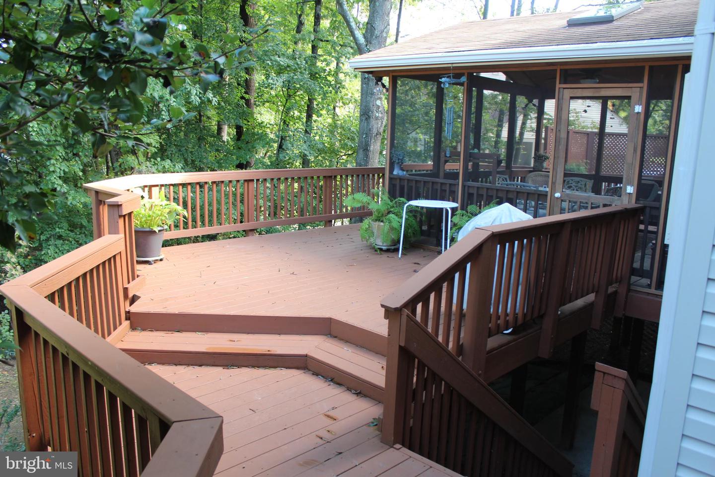 Multi-level deck with steps and railings beside a screened porch, surrounded by trees.