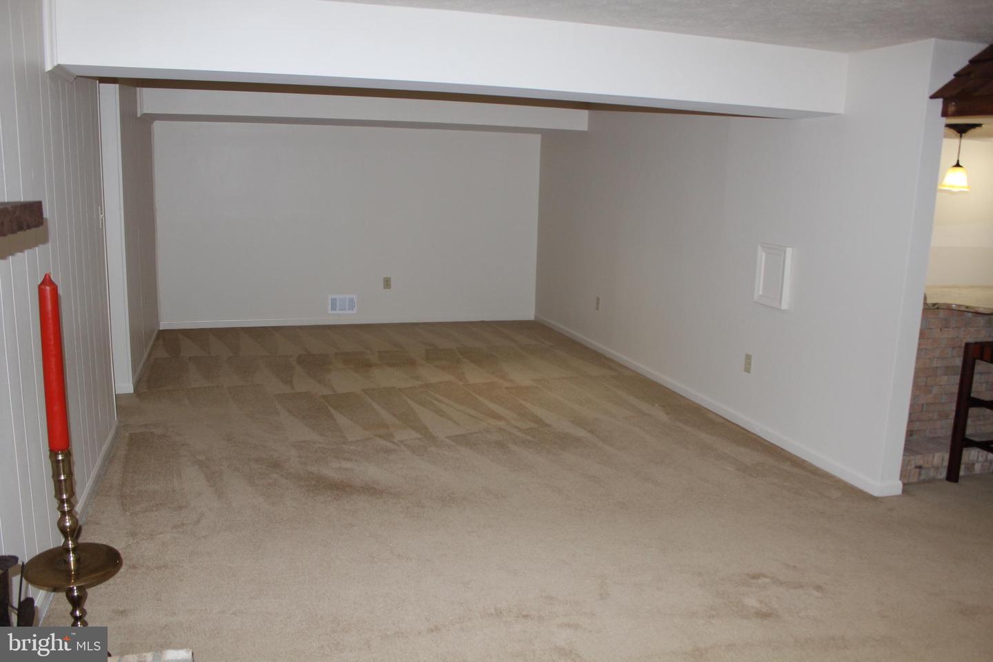 Empty carpeted room with white walls, paneled wall, and a partial brick fireplace.