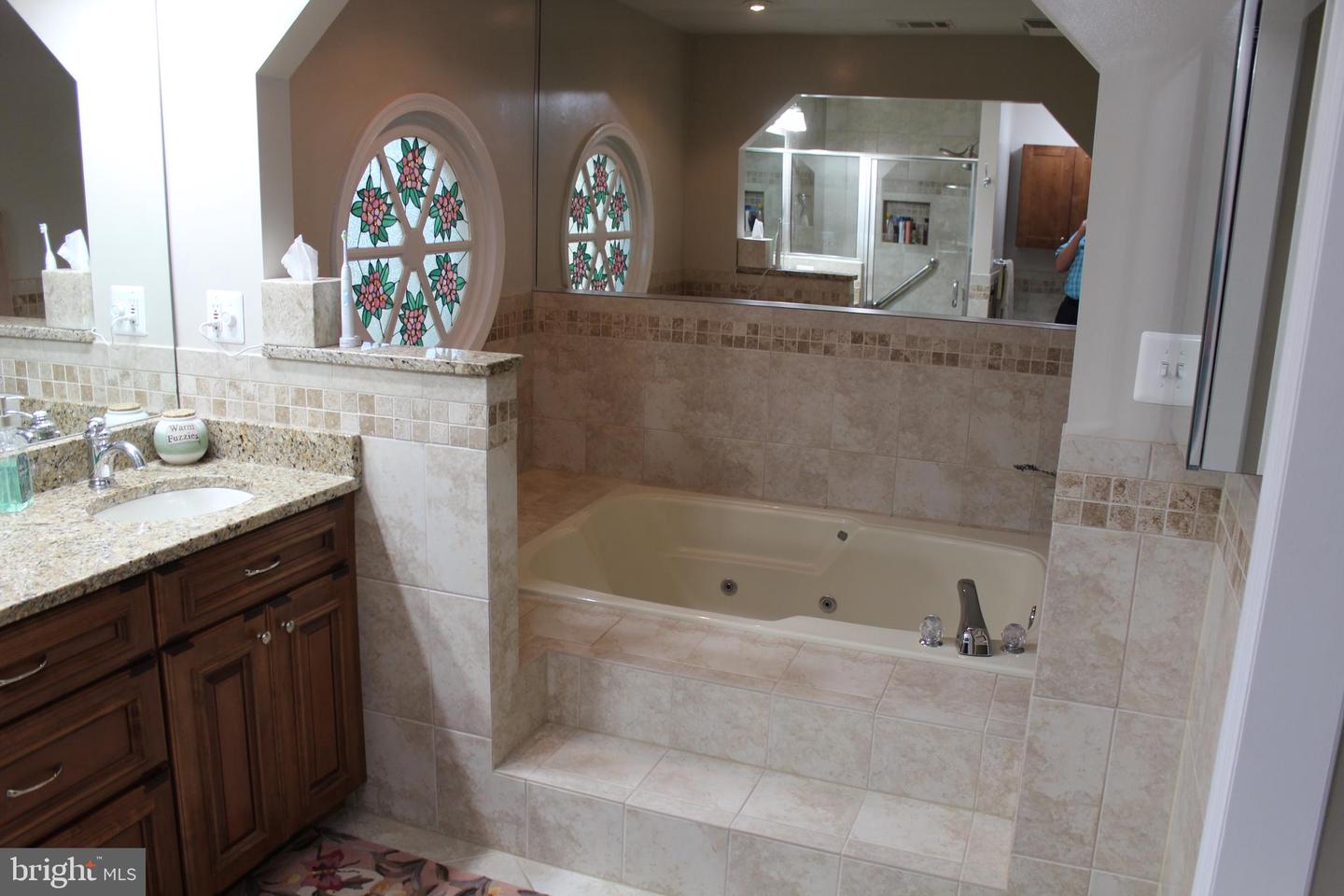 Bathroom with a jetted tub, glass shower, dark wood vanity, and floral stained-glass windows.