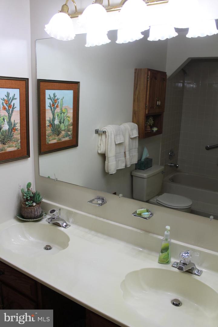 Bathroom with a double-sink vanity, large mirror, and tub-shower reflected behind it.