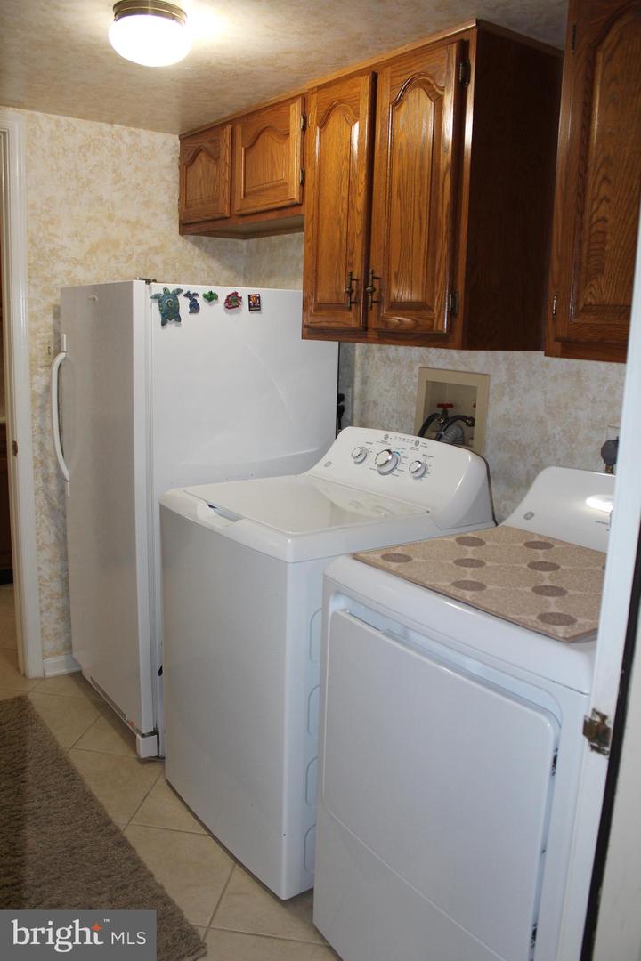 Laundry room with washer, dryer, refrigerator, and oak cabinets.