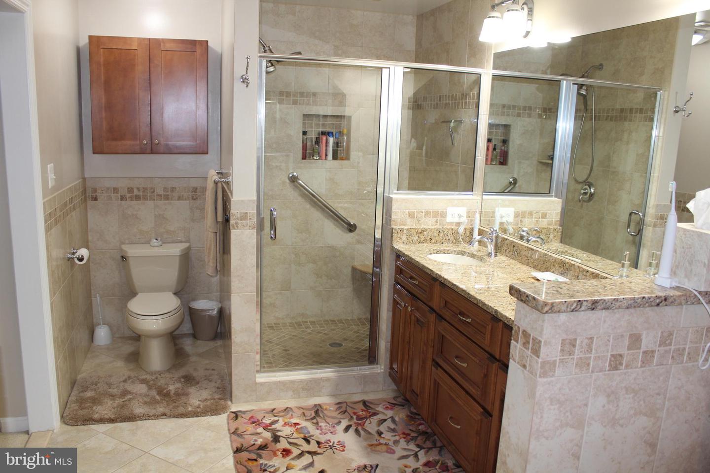 Tiled bathroom with a glass walk-in shower, grab bars, and a dark wood vanity with granite countertop.