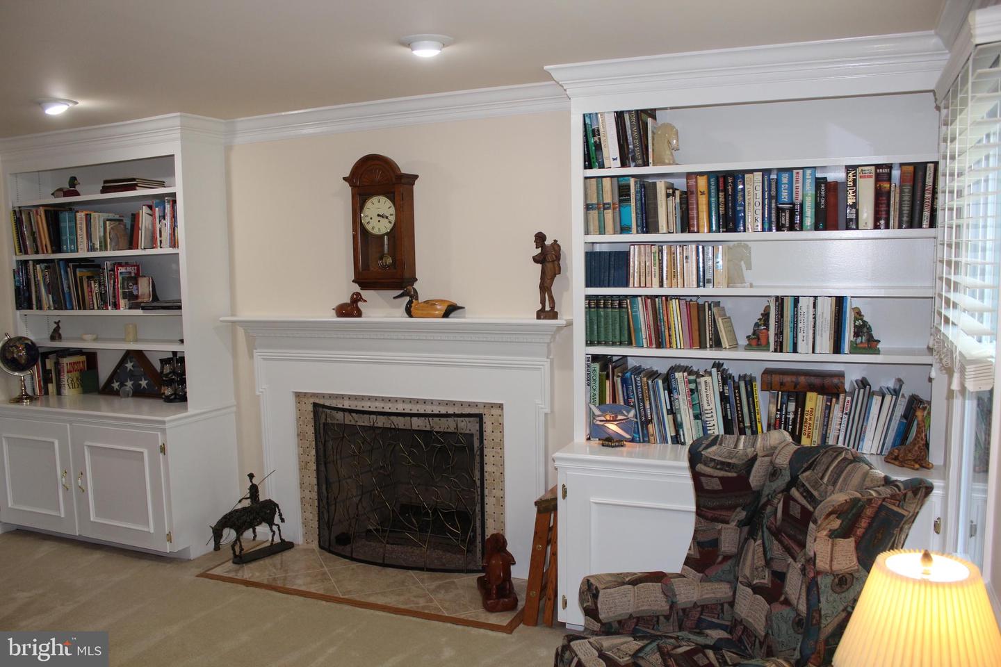 Living room with a white fireplace, wall-to-wall bookcases, and patterned armchairs.