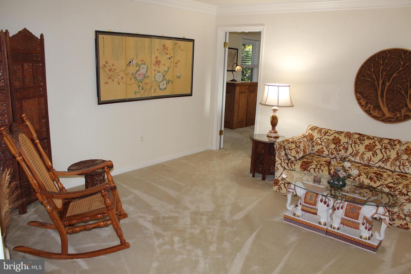 Living room with a floral sofa, carved rocking chair, beige carpet, and framed floral artwork.