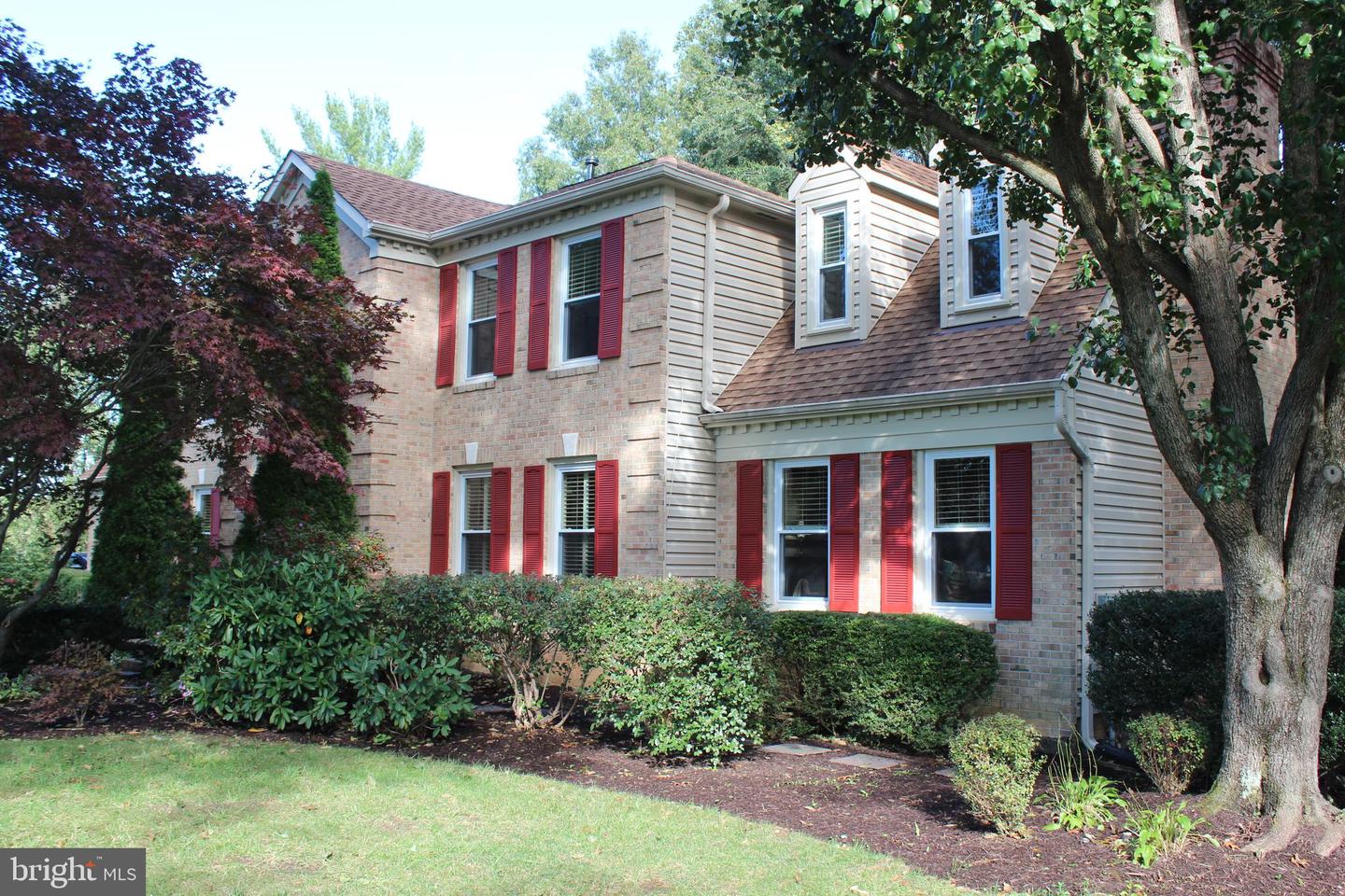 Two-story brick house with red shutters, dormers, and mature trees.