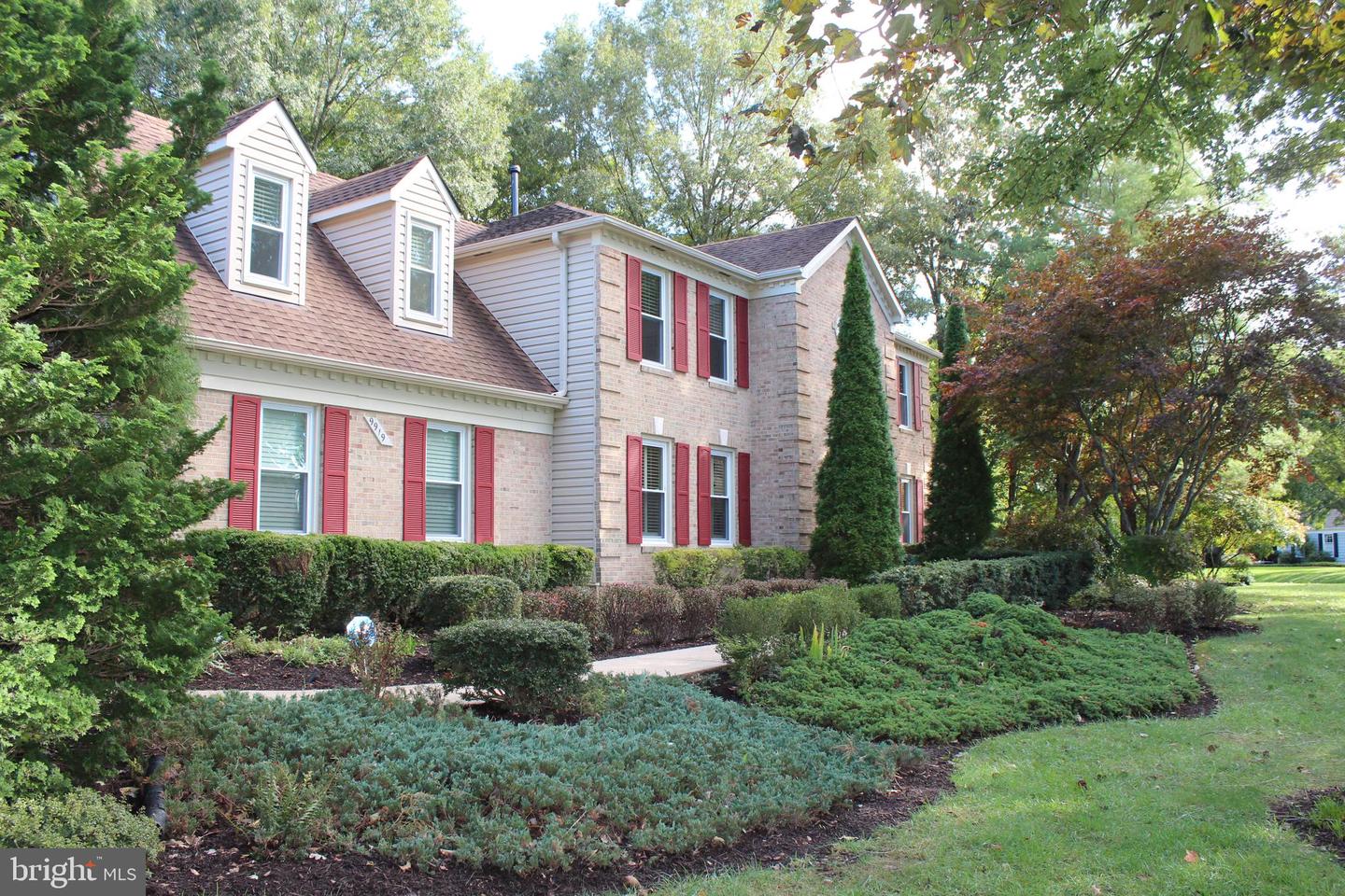 Two-story brick house with red shutters, roof dormers, and landscaped front yard.