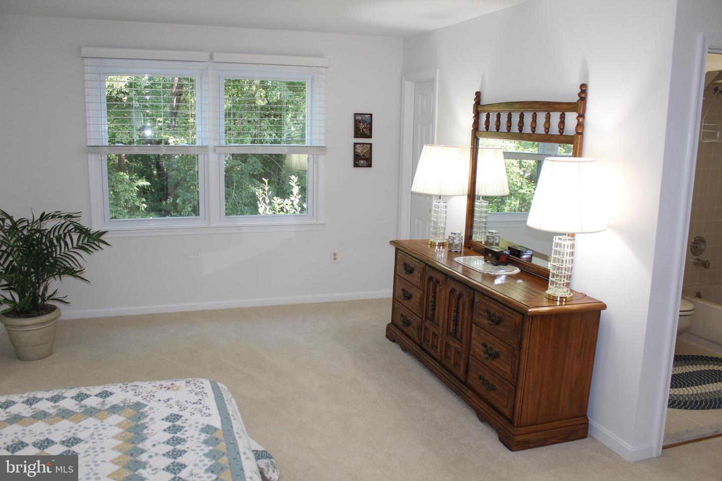 Bedroom with carpet, wooden dresser and mirror, and windows overlooking trees.