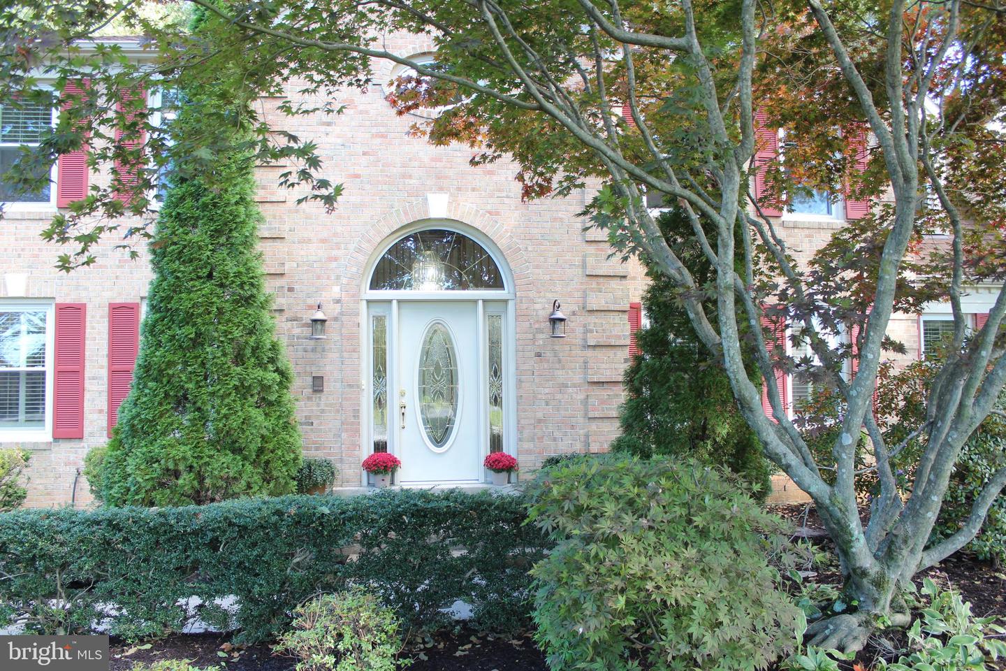 Brick house entrance with red shutters, an arched window, and a white oval-glass front door.